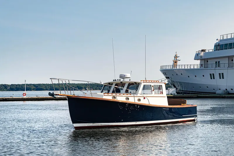 Slide: The Image of 1985 Wilbur 34 boat cruising in a marina, clear sky, large ship in background. - 2