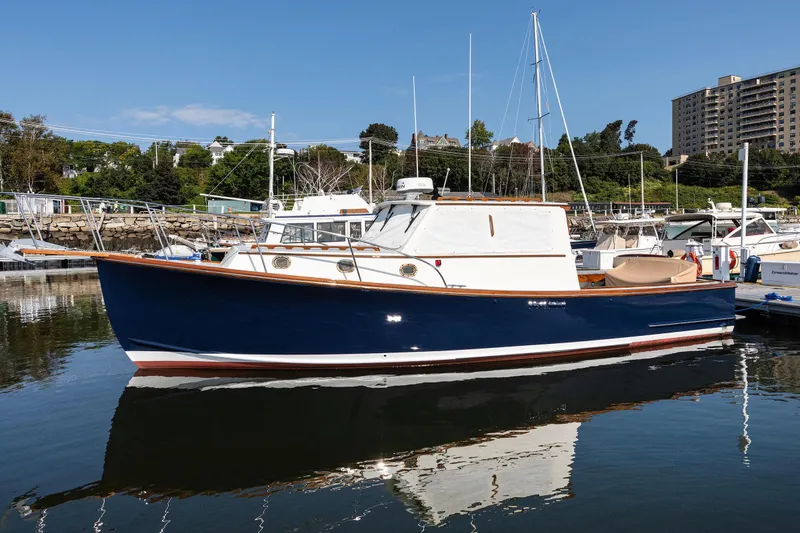 Slide: The Image of 1985 Wilbur 34 boat docked in marina, blue hull, white cabin, clear sky background. - 23