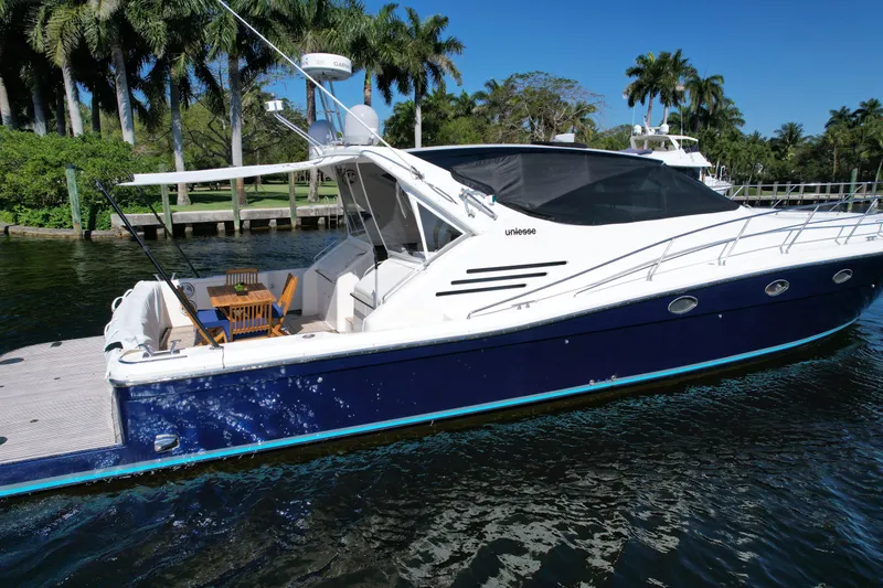 Slide: The Image of 1999 Uniesse 57 Open yacht docked on a sunny day, surrounded by palm trees. - 10