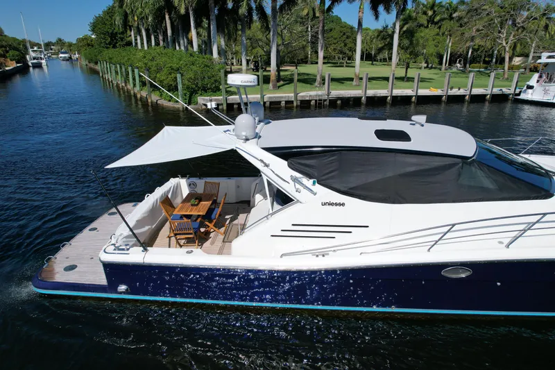 Slide: The Image of 1999 Uniesse 57 Open yacht cruising on a scenic waterway with lush greenery. - 7