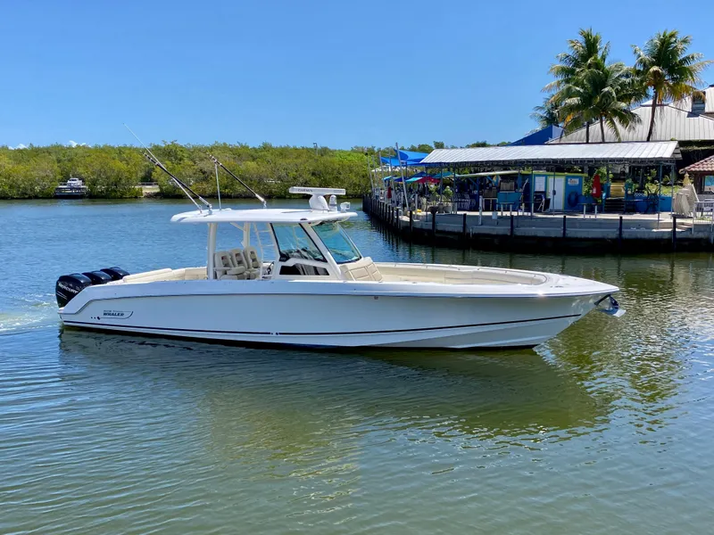 Slide: The Image of 2019 Boston Whaler 380 Outrage boat on calm water near a dockside restaurant. - 5