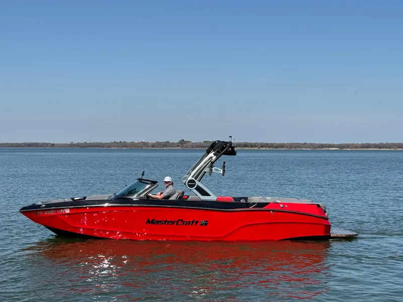 The Image of 2022 MasterCraft XT24 boat in vibrant red on a calm lake. - 0