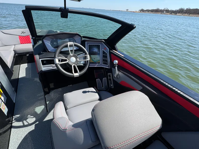 Slide: The Image of 2022 MasterCraft XT24 boat interior with modern dashboard and steering wheel on a lake. - 10