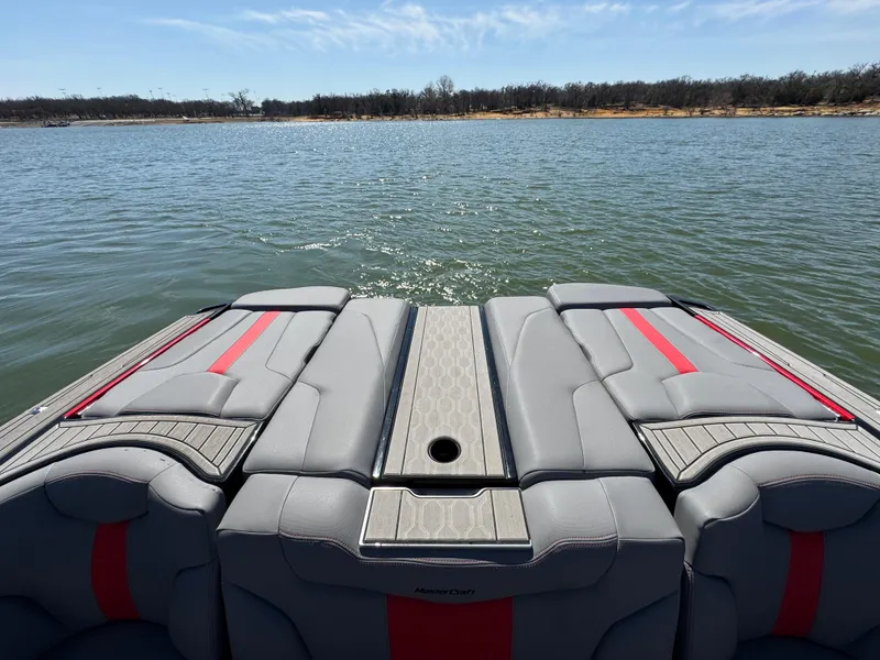 Slide: The Image of 2022 MasterCraft XT24 boat interior with gray and red seating on a lake. - 21