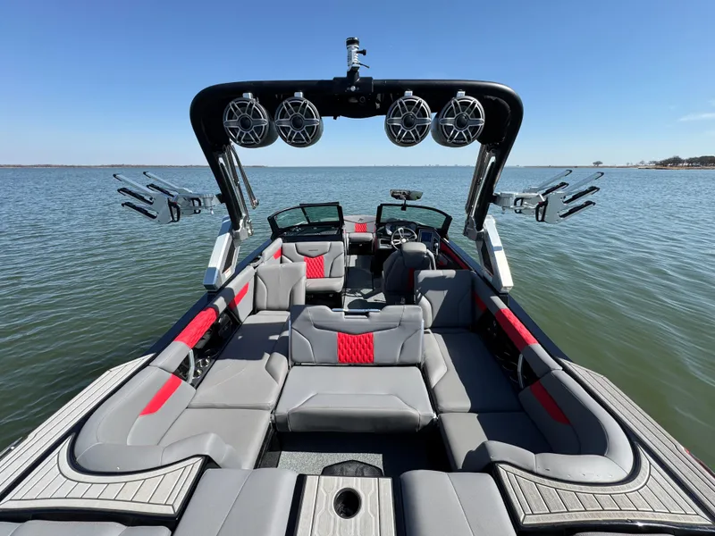Slide: The Image of 2022 MasterCraft XT24 boat interior with speakers, gray and red seating, on a calm lake. - 22