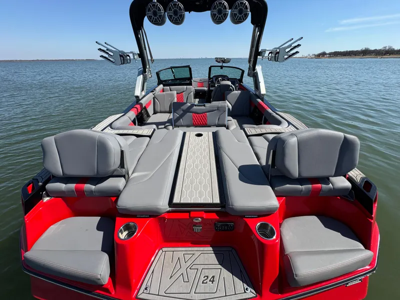 Slide: The Image of 2022 MasterCraft XT24 boat with red and gray seating on a calm lake. - 23