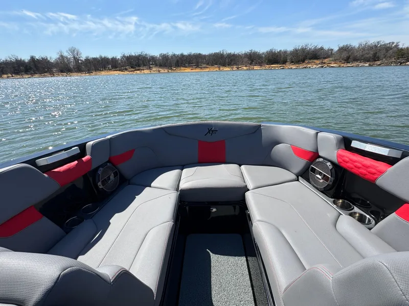 Slide: The Image of 2022 MasterCraft XT24 boat interior with gray and red seating on a lake. - 5