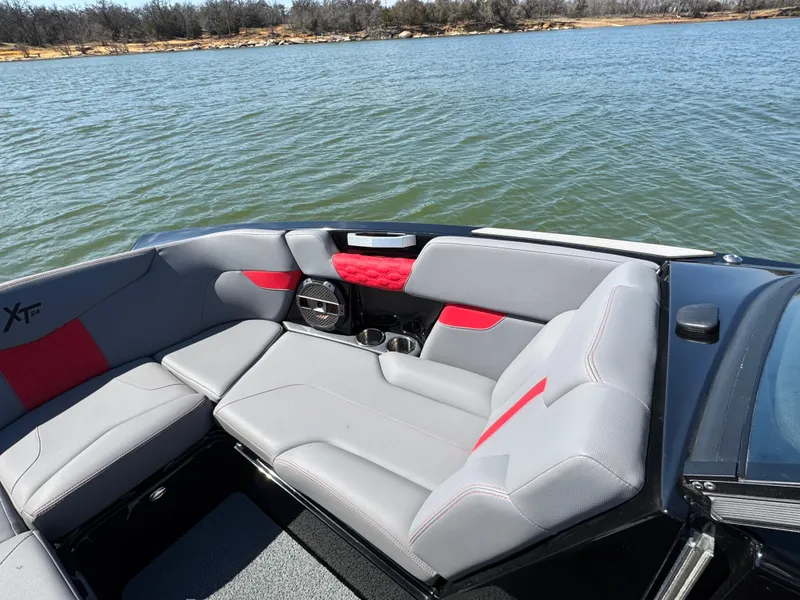 Slide: The Image of 2022 MasterCraft XT24 boat interior with gray and red seating on a lake. - 6
