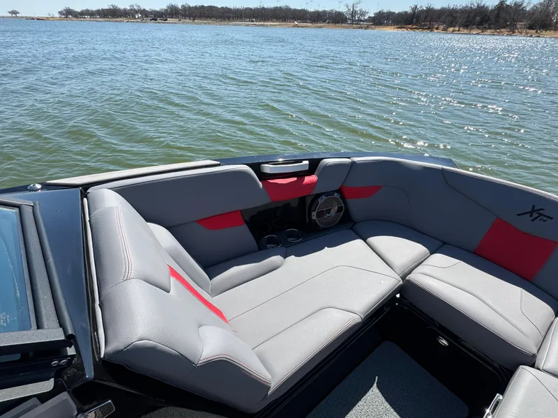 Slide: The Image of 2022 MasterCraft XT24 boat interior with gray and red seating on a lake. - 7