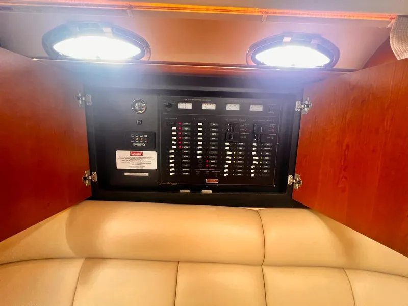 Slide: The Image of 2001 Cruisers Yachts 3870 Express electrical panel in wooden cabinet with cushioned seating. - 18
