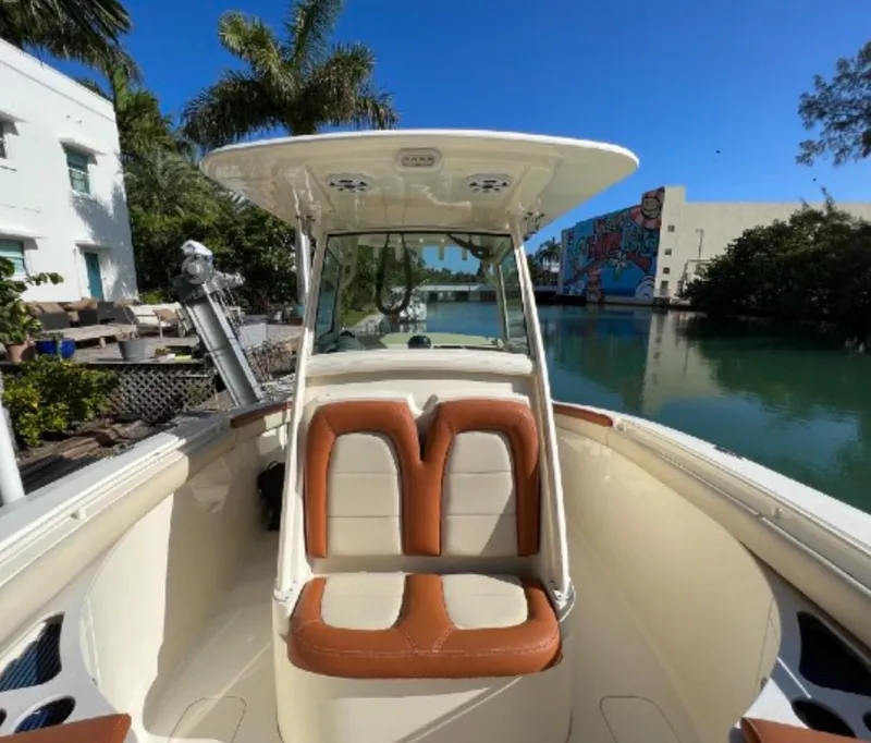 Slide: The Image of 2013 Scout 275 LXF boat with tan seating, docked by a canal under clear blue skies. - 12