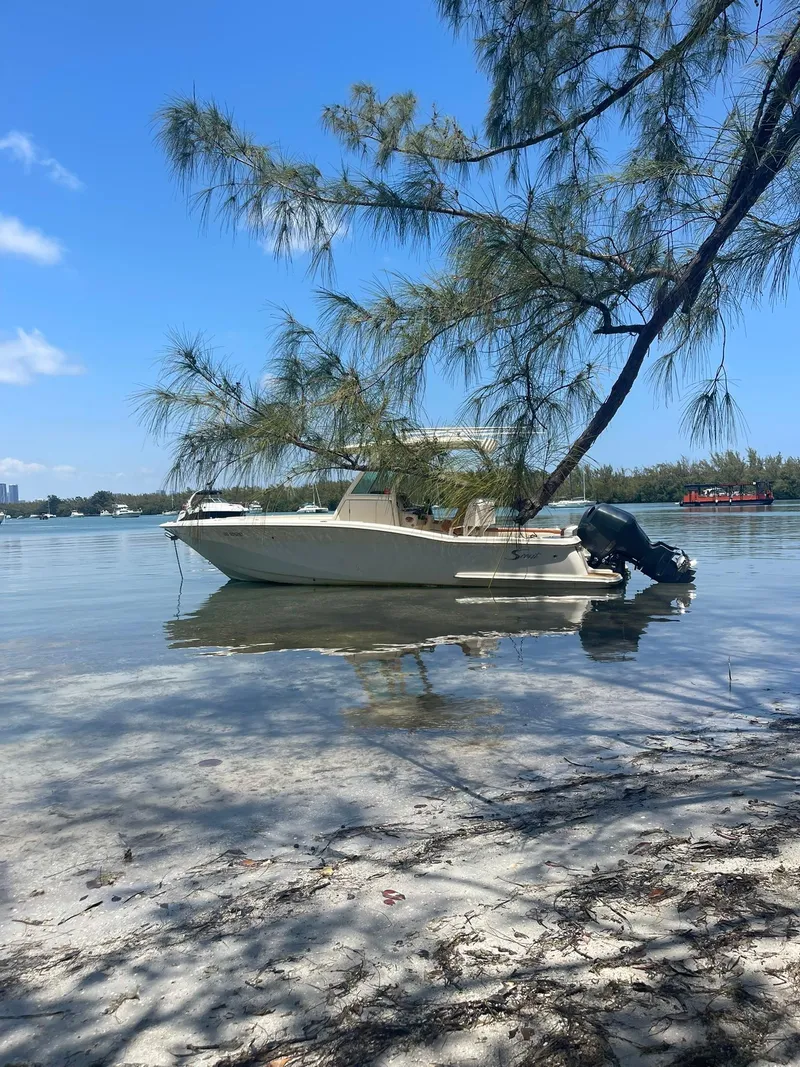 Slide: The Image of 2013 Scout 275 LXF boat anchored near a sandy shore under a clear blue sky. - 21