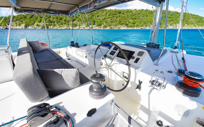 Slide: The Image of Lagoon 450F 2015 catamaran cockpit with steering wheel, ocean view, and lush green shoreline. - 17