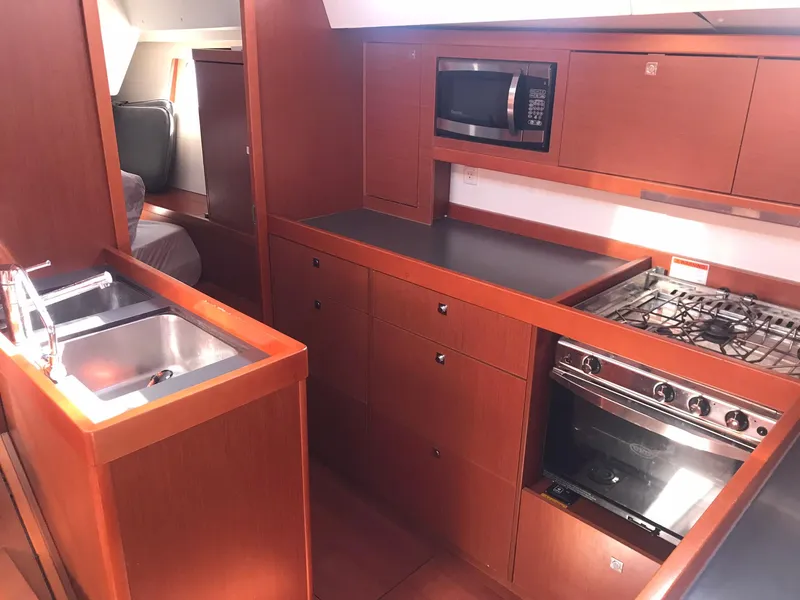 Slide: The Image of 2014 Beneteau Oceanis 48 yacht kitchen with wood cabinetry, stove, microwave, and sink. - 30