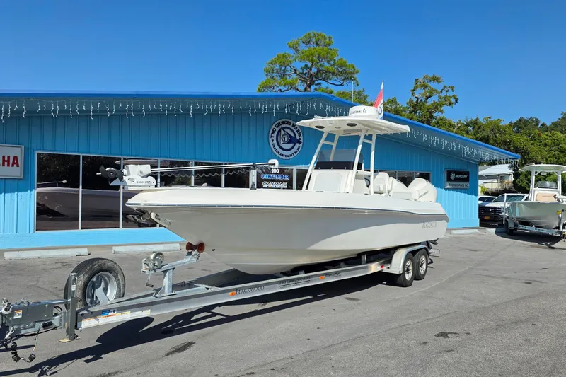 Slide: The Image of 2021 Blackwood 27 boat on trailer, parked outdoors near palm trees and a blue building. - 0