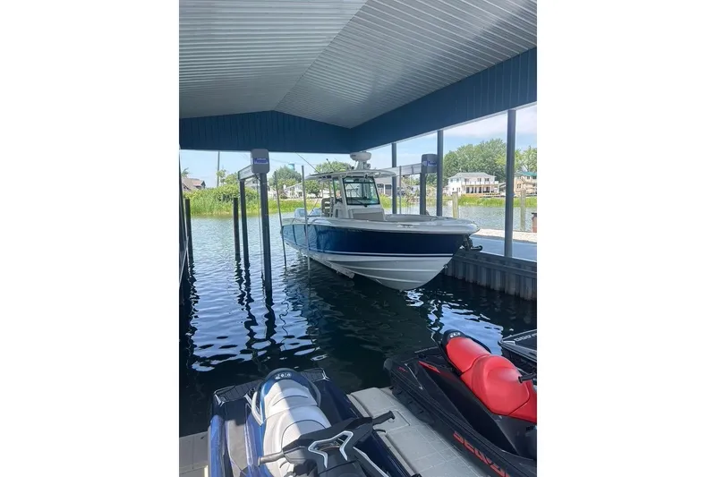 Slide: The Image of 2016 Boston Whaler 330 Outrage docked in covered marina with jet skis nearby. - 2