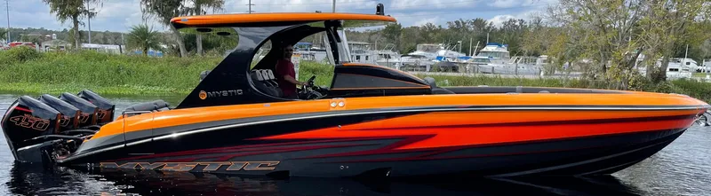 Slide: The Image of 2023 Mystic Powerboats M3800, sleek orange and black design, cruising on a calm waterway. - 10