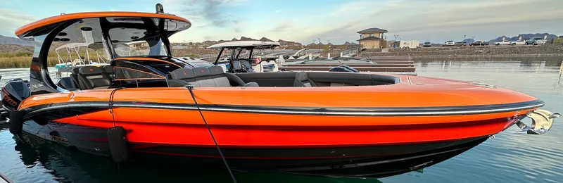 Slide: The Image of 2023 Mystic Powerboats M3800, vibrant orange, docked on calm water. - 11