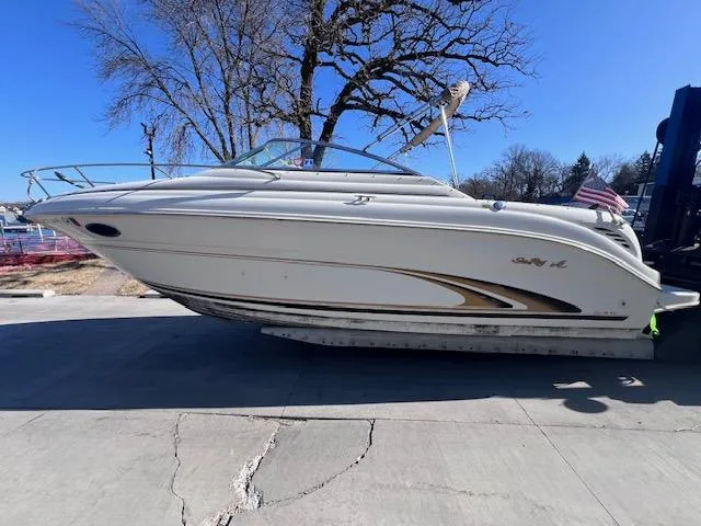 The Image of 2000 Sea Ray 245 Weekender boat on trailer, parked outdoors under clear blue sky. - 0