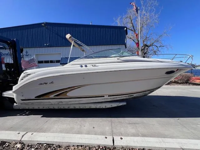 Slide: The Image of 2000 Sea Ray 245 Weekender boat on trailer, parked near a blue building. - 3