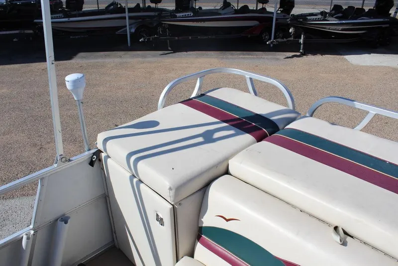 Slide: The Image of 1997 Monark Pontoon boat seating with striped upholstery, parked on gravel. - 14
