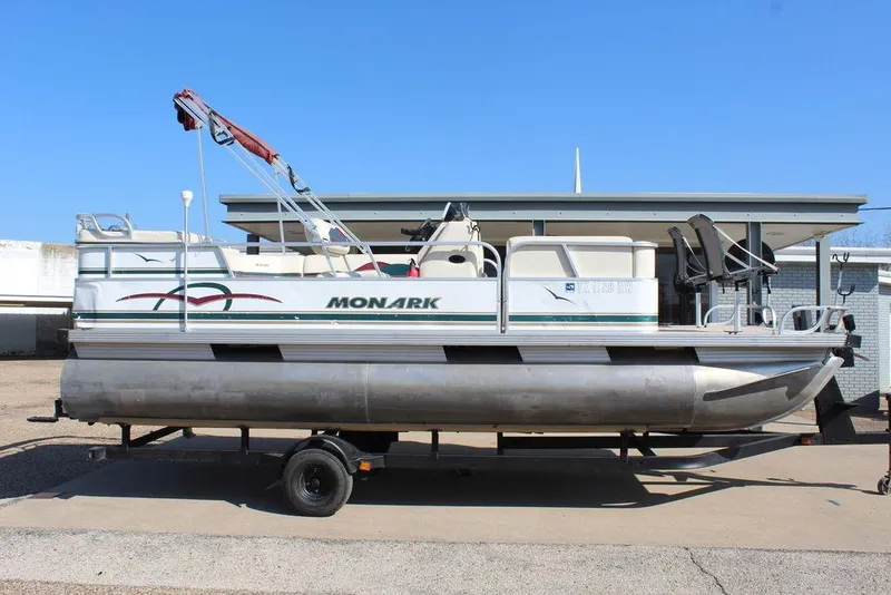 Slide: The Image of 1997 Monark Pontoon boat on trailer, parked outdoors, clear blue sky background. - 3