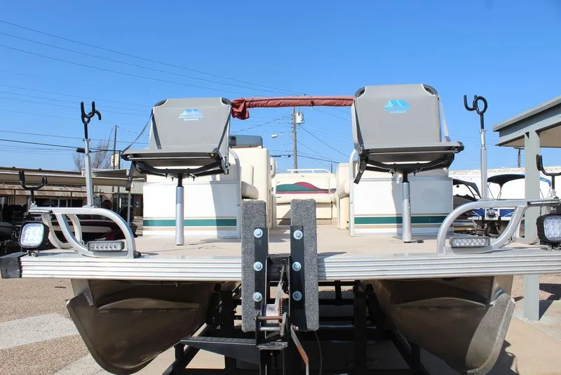 Slide: The Image of 1997 Monark Pontoon boat with dual fishing seats and rod holders, parked on a trailer. - 7