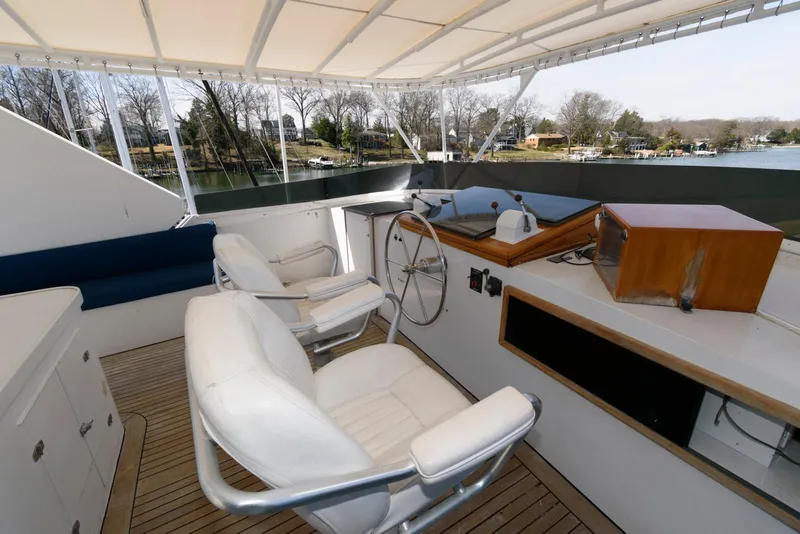 Slide: The Image of 1984 Broward 100 yacht helm with white seating and wooden accents, docked by a serene waterfront. - 12