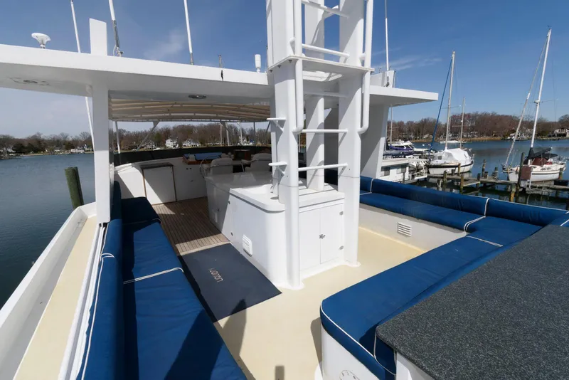 Slide: The Image of Deck view of 1984 Broward 100 yacht with blue seating and marina backdrop. - 15
