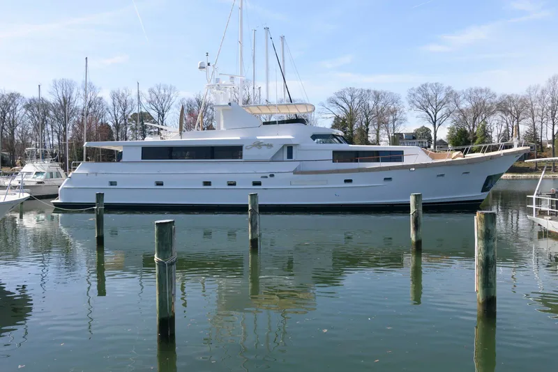 Slide: The Image of 1984 Broward 100 yacht docked in a serene marina setting. - 2