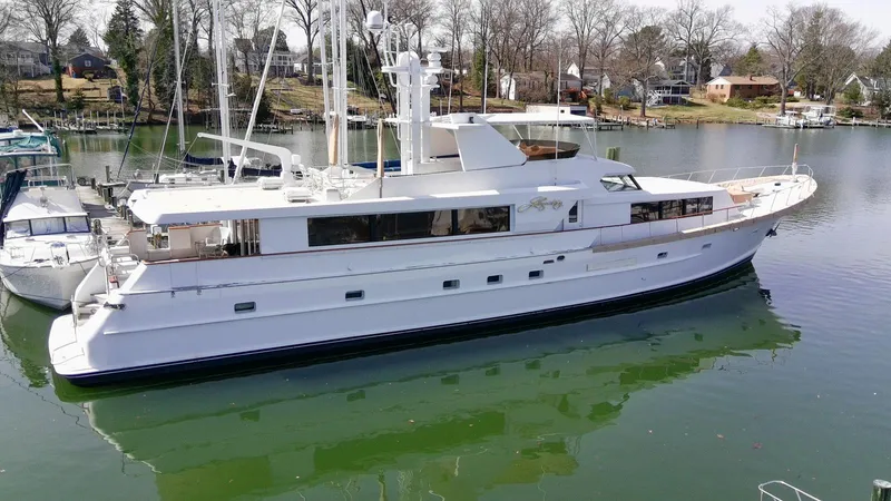 Slide: The Image of Luxurious 1984 Broward 100 yacht docked on calm waters, surrounded by trees and houses. - 3