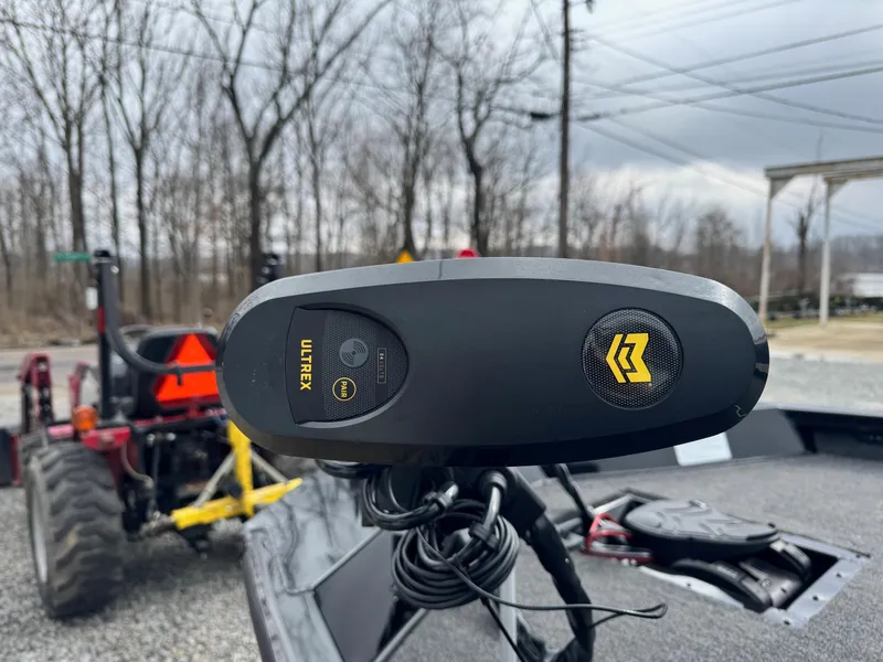 Slide: The Image of 2025 Crestliner XF189 boat with Ultrex trolling motor, parked near a tractor on a gravel path. - 8