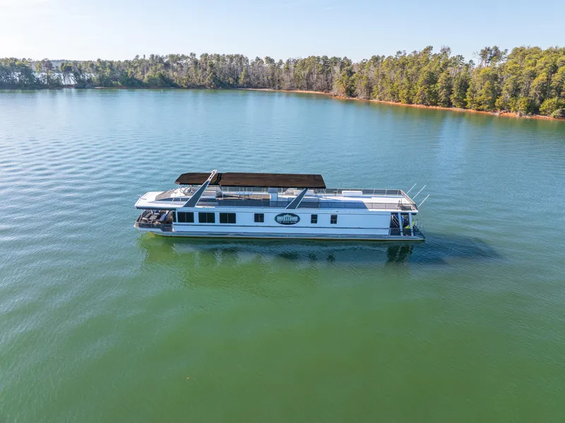 The Image of 1998 Stardust Cruisers Custom Luxury Houseboat on serene lake with forested shoreline. - 1