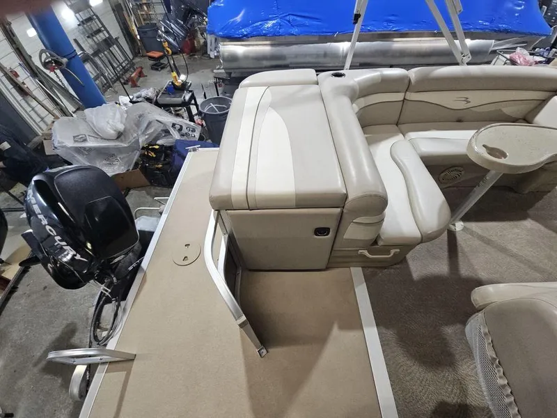 Slide: The Image of 2012 Bennington 20SL pontoon boat interior with beige seating and motor in a workshop. - 8