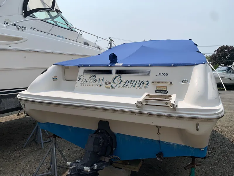 Slide: The Image of 2000 Sea Ray 215 Express Cruiser with blue cover, docked outdoors. - 2