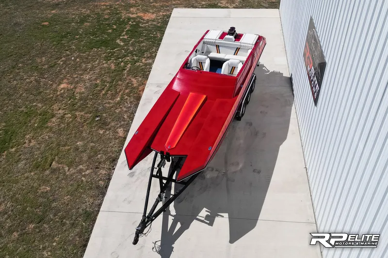 Slide: The Image of Red 1998 Warlock 28 SXT speedboat parked on concrete near a building. - 10