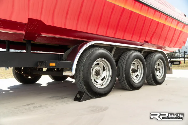 Slide: The Image of Red 1998 Warlock 28 SXT boat on a triple-axle trailer, parked on concrete. - 33