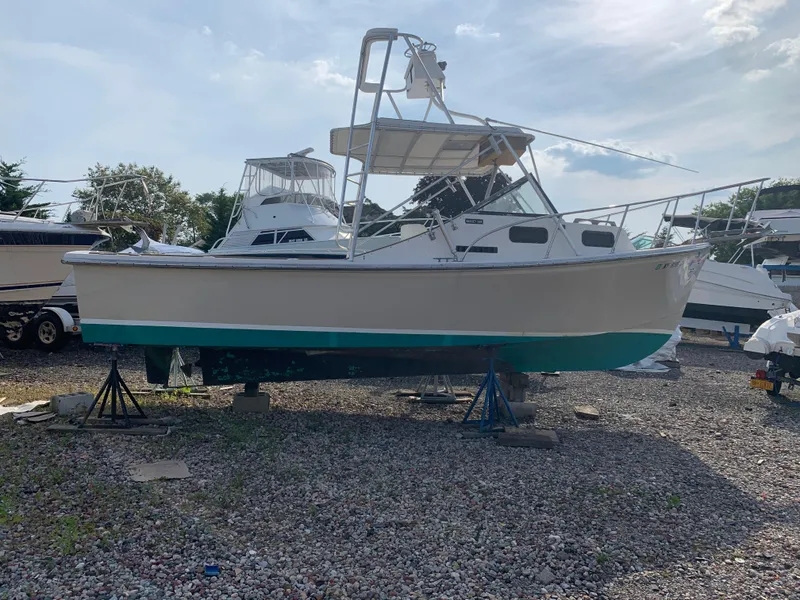 Slide: The Image of 1987 Nauset 249 boat on stands in a gravel yard, with other boats nearby. - 0
