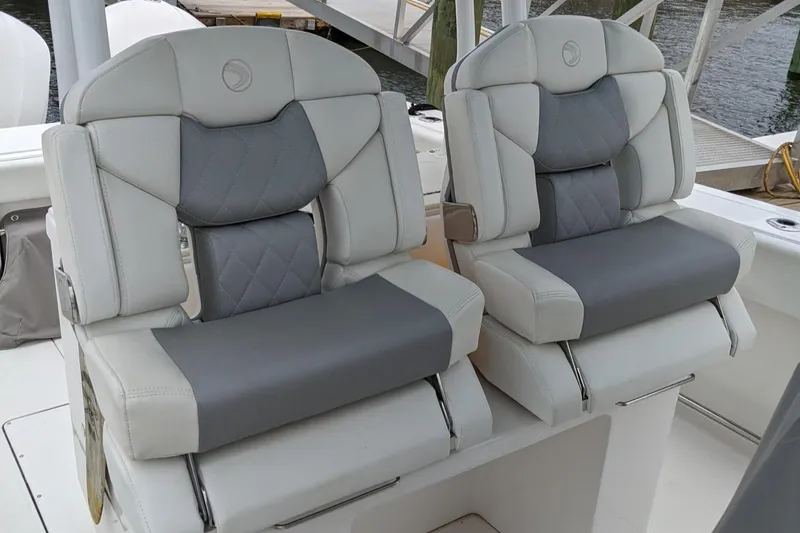 Slide: The Image of 2018 Edgewater 320 CC boat seats, featuring gray and white cushioned design, dockside view. - 8