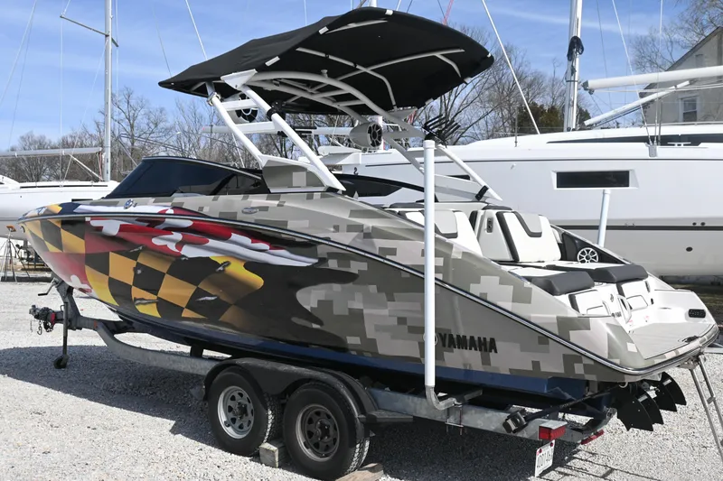 Slide: The Image of 2023 Yamaha Boats 252SD with custom graphics on a trailer, parked outdoors. - 6