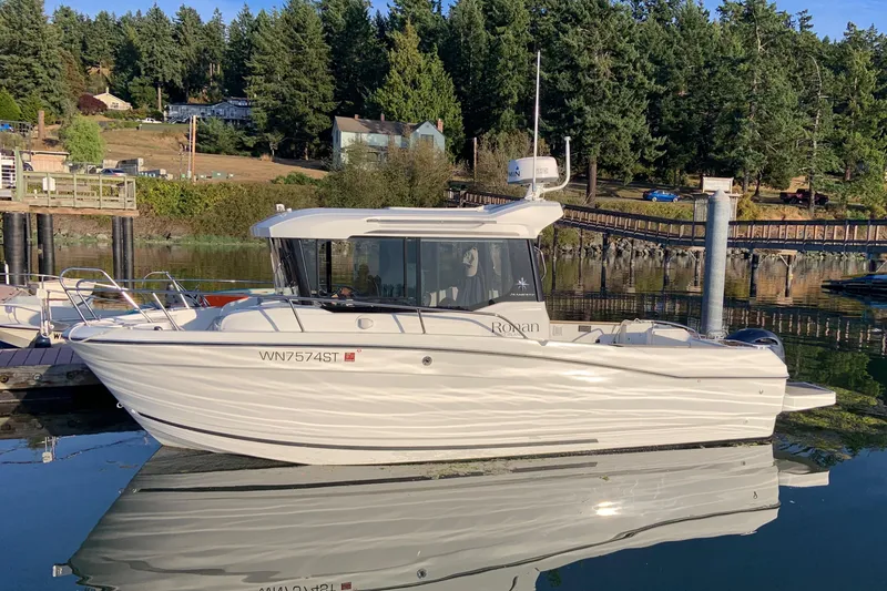 Slide: The Image of 2020 Jeanneau NC Sport 695 boat docked on calm water, surrounded by trees. - 0