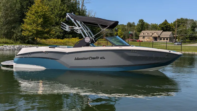 Slide: The Image of 2025 MasterCraft NXT23 boat on a calm lake with trees and houses in the background. - 3
