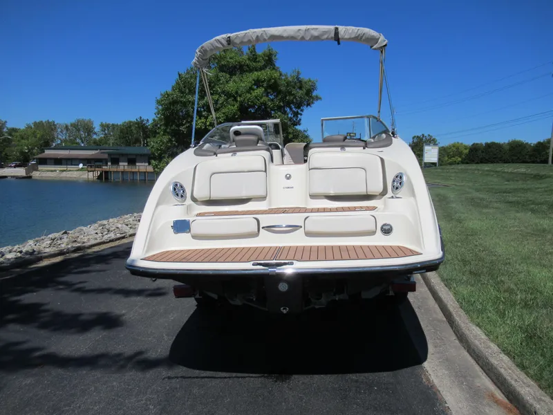 Slide: The Image of 2014 Yamaha Boats 242 Limited, rear view, parked near a lake on a sunny day. - 2