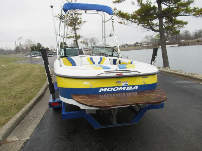 Slide: The Image of 2000 Moomba Outback LS boat with vibrant yellow and blue design, parked near a lake. - 2