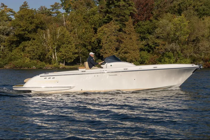 Slide: The Image of 2022 Comitti Isola I-33 boat cruising on a serene lake with lush forest backdrop. - 2