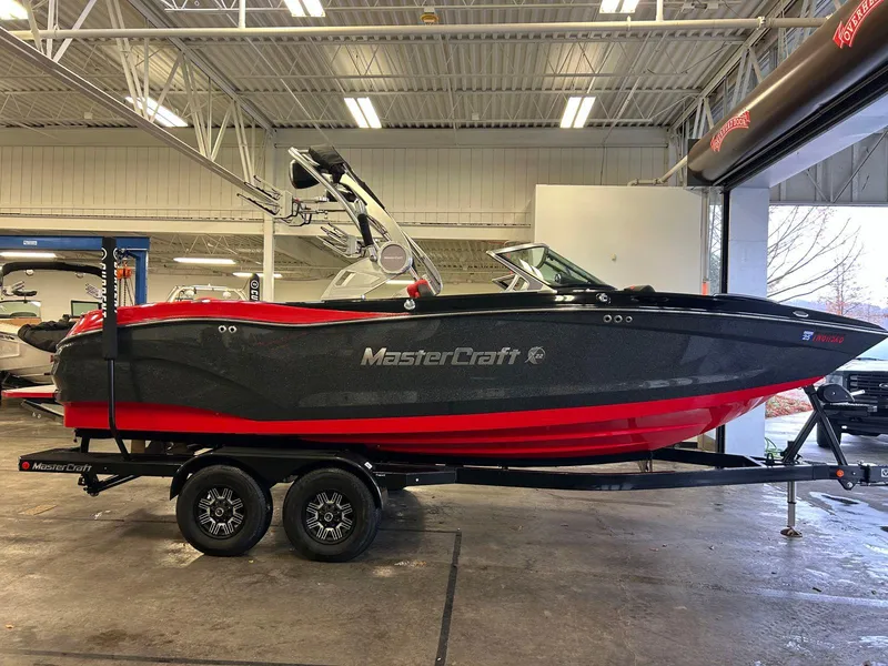 Slide: The Image of 2020 MasterCraft X22 boat in showroom, black and red design, on a trailer. - 2
