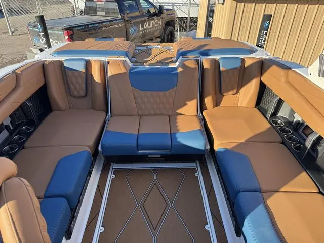 Slide: The Image of 2025 Malibu M230 boat interior with tan and blue seating, featuring cup holders and spacious layout. - 10