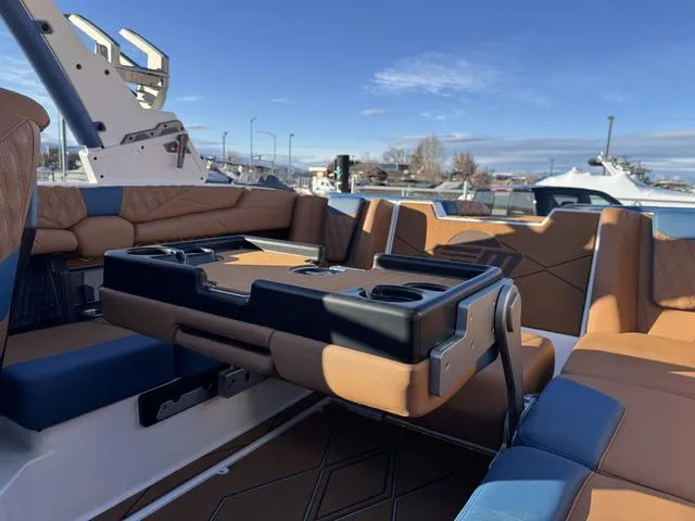 Slide: The Image of 2025 Malibu M230 boat interior with tan and blue seating, featuring a foldable table. - 15