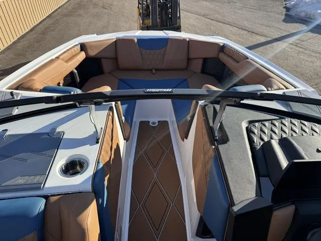 Slide: The Image of 2025 Malibu M230 boat interior with tan and blue seating, cup holder, and diamond-pattern flooring. - 21
