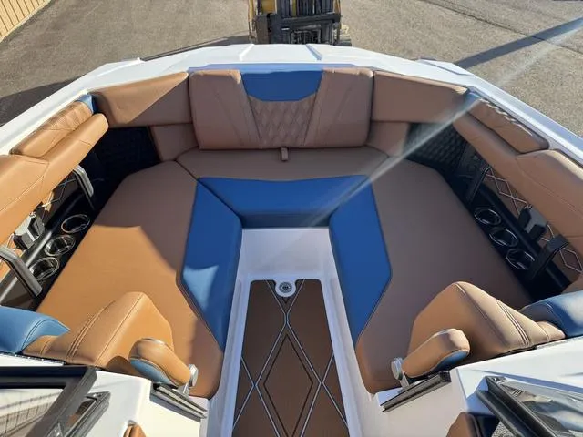 Slide: The Image of 2025 Malibu M230 boat interior with brown and blue seating, cup holders, and diamond-patterned flooring. - 22
